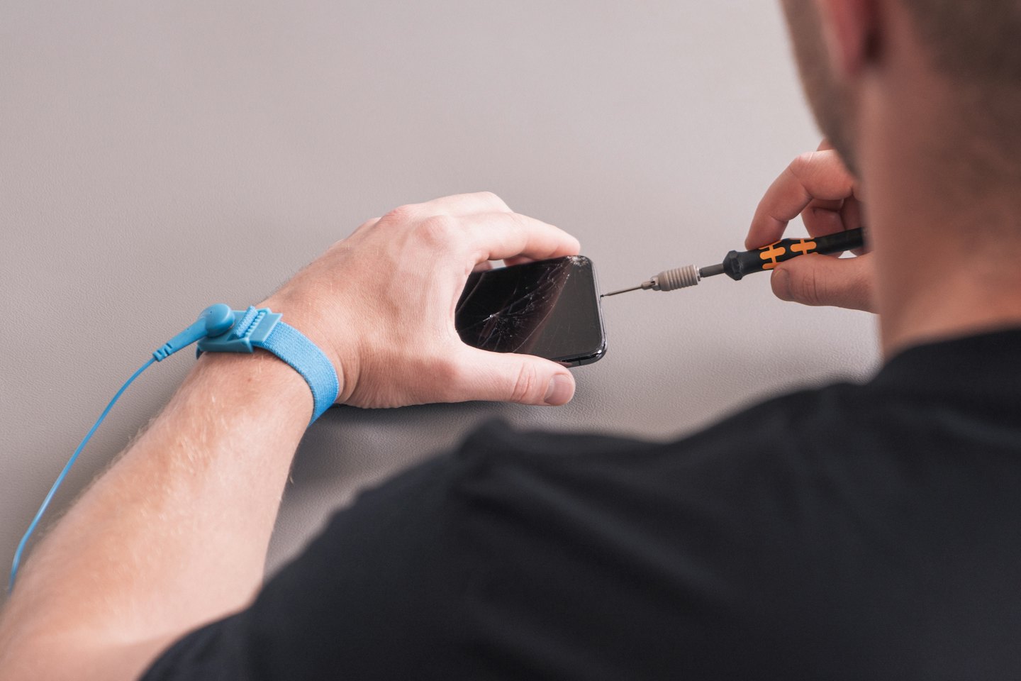 Persona ripara uno schermo di smartphone rotto con un cacciavite di precisione.
